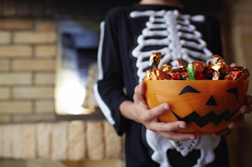 child in skeleton costume holding bucket of candy