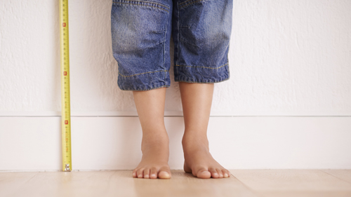 child standing up against a wall with measuring tape