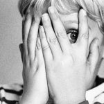 black and white photo of a little boy covering his face while peeking through his hands