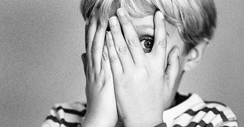 black and white photo of a little boy covering his face while peeking through his hands