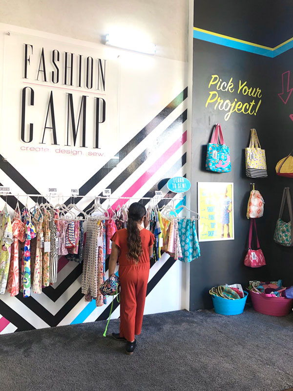 A child looks through a clothing rack as the words "Fashion Camp" appear over their head