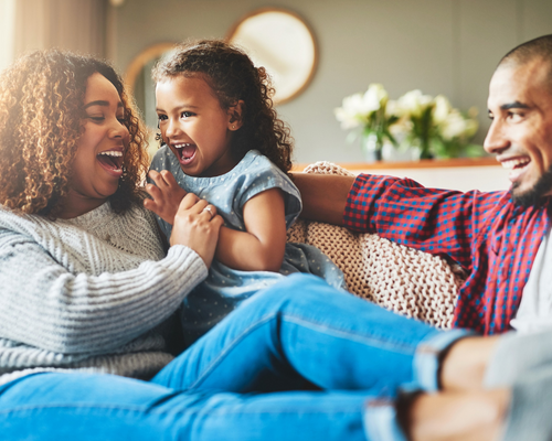 Mother father and daughter sitting on a couch laughing Mindfulness