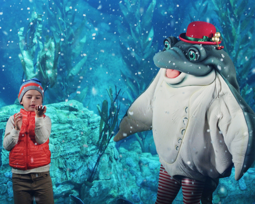 Boy and Sea Animal Mascot dressed in Christmas attire infant of an aquarium.
