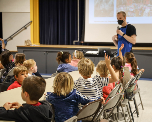 A teacher talking on a microphone while giving a presentation to his class.