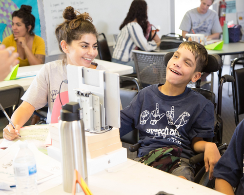 a smiling woman teaching something to a smiling kid