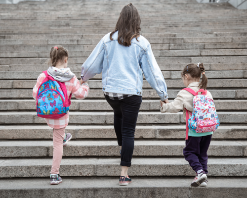 Mom walking her two young daughters with backpacks up school steps