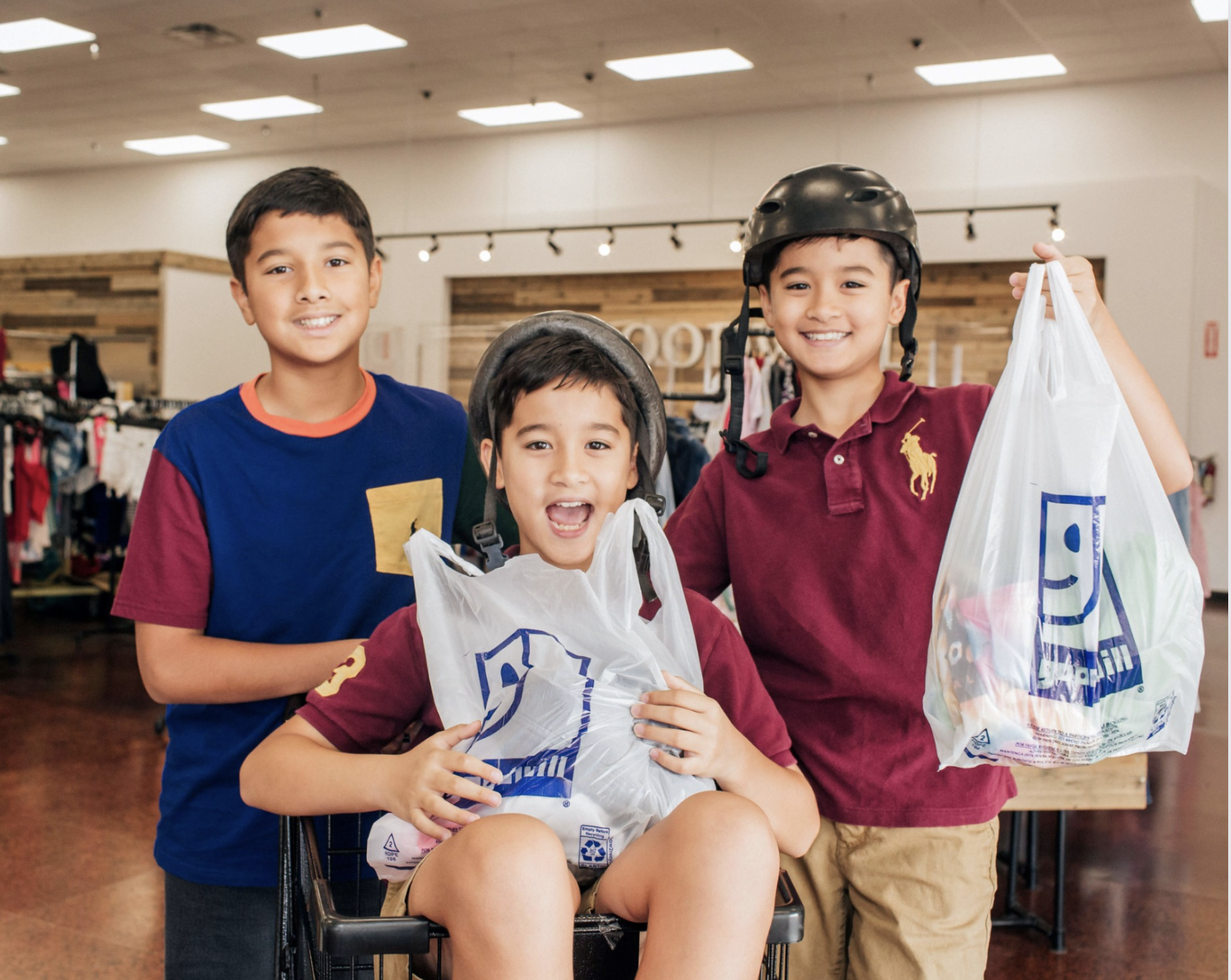 Three boys holding bags of clothes and wearing helmets at Goodwill OC Best Kids Resale Clothing