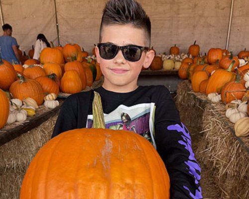 A boy in sunglasses holding a huge pumpkin at the Pumpkin Factory Pumpkin Patch