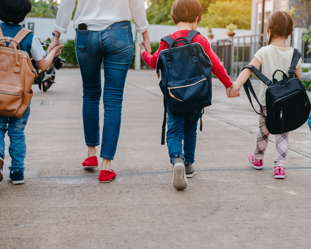 mom walking little kids with their backpacks on to school