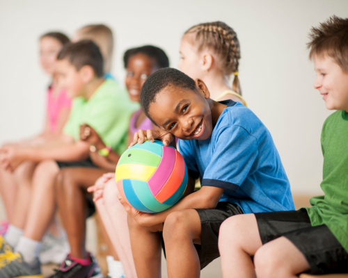 young boy smiling holding a colorful volleyball