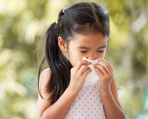 girl sneezing into a tissue