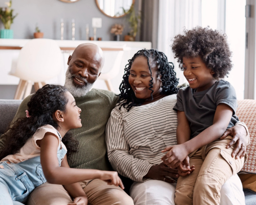 Family of four smiling, sitting on a couch together