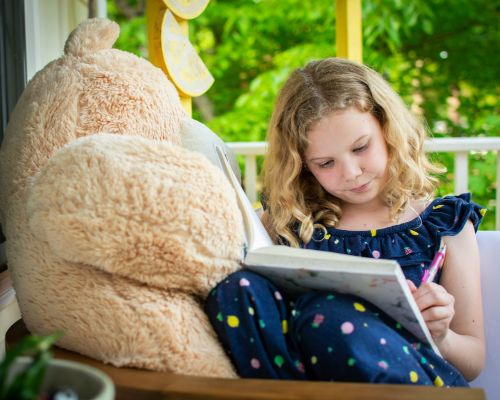 little girl reading a book next to a teddy bear