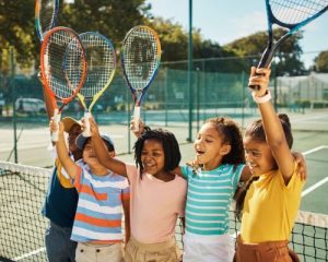 Kids holding up tennis rackets on a tennis court cheering and connecting