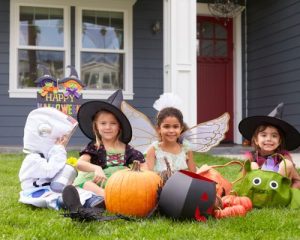 four kids in halloween costumes sitting on the lawn with trick or treating bags and pumpkins